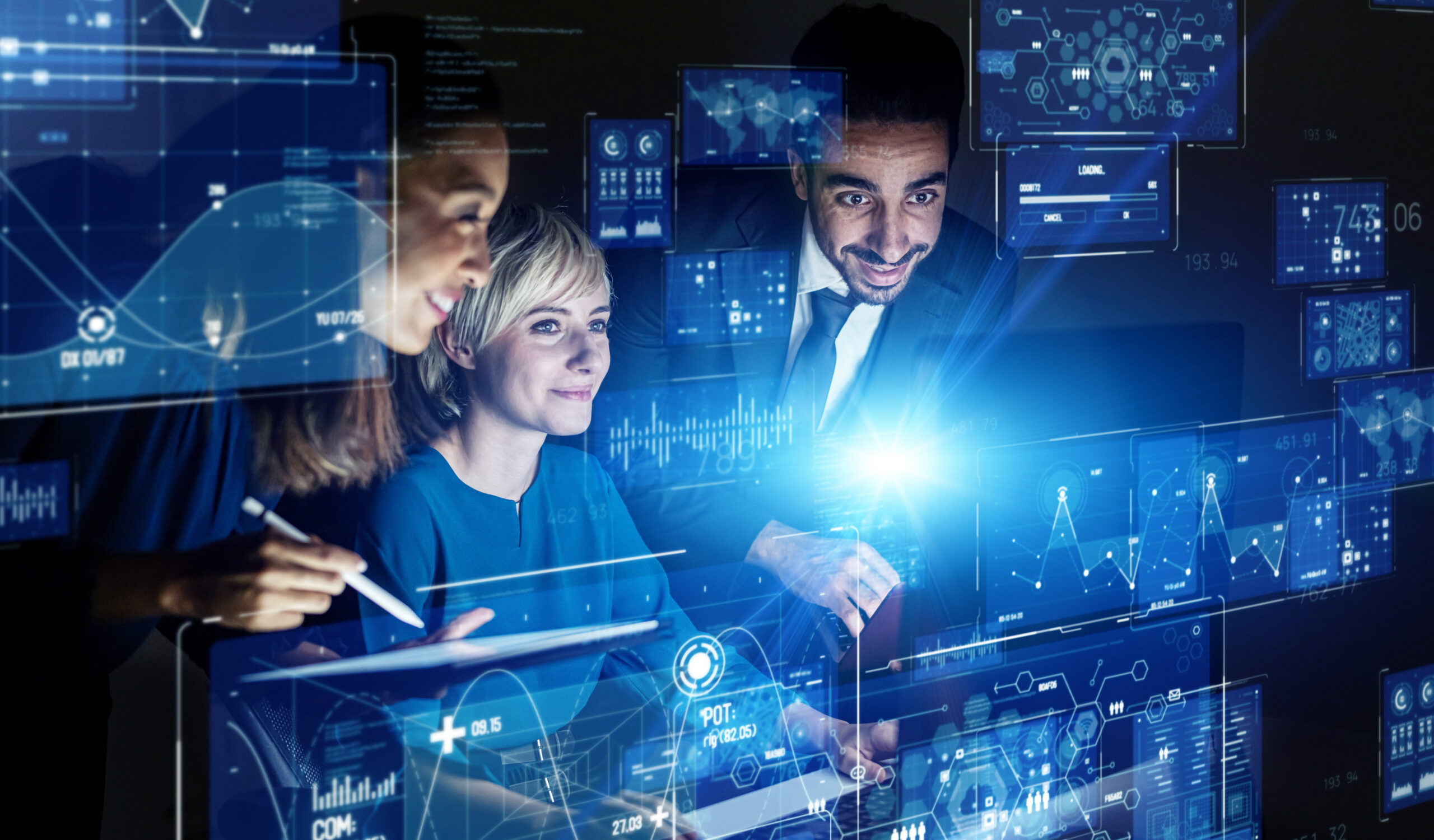 Three smiling professionals gathered around a laptop and tablet, surrounded by glowing holographic data dashboards and charts